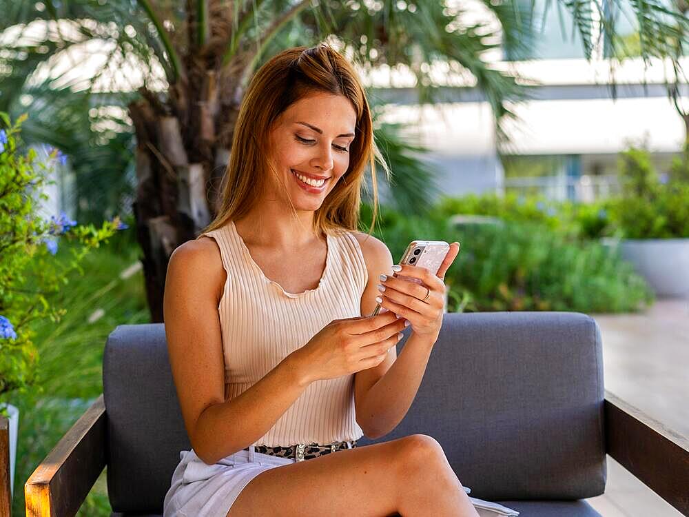 Smiling woman is sitting on a sofa while she turns off her smartphone