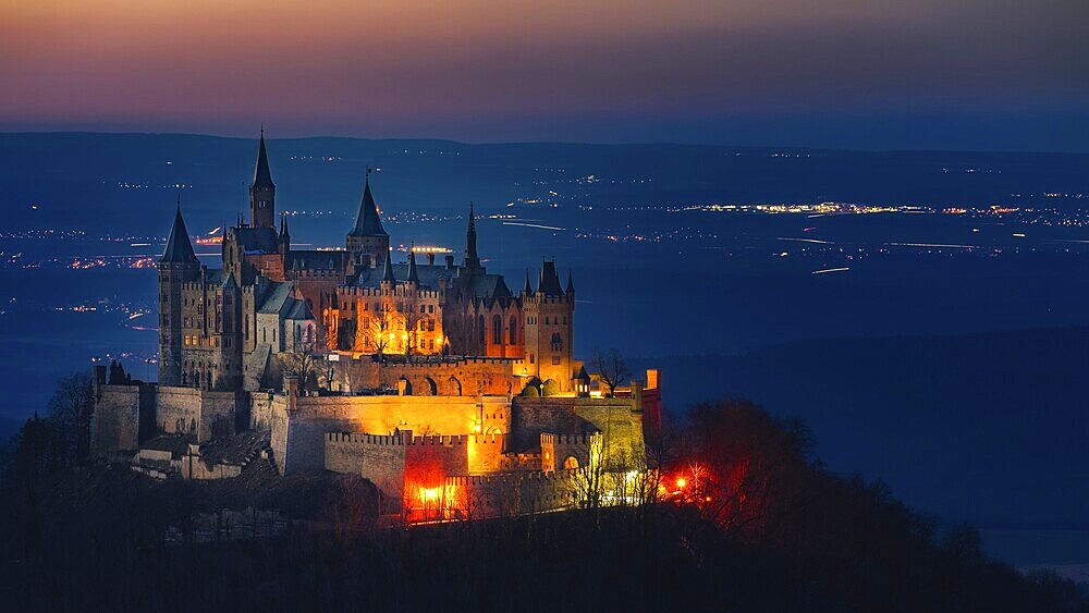 Hohenzollern Castle, the ancestral seat of the House of Hohenzollern, photographed in the evening with the illuminated villages in the background