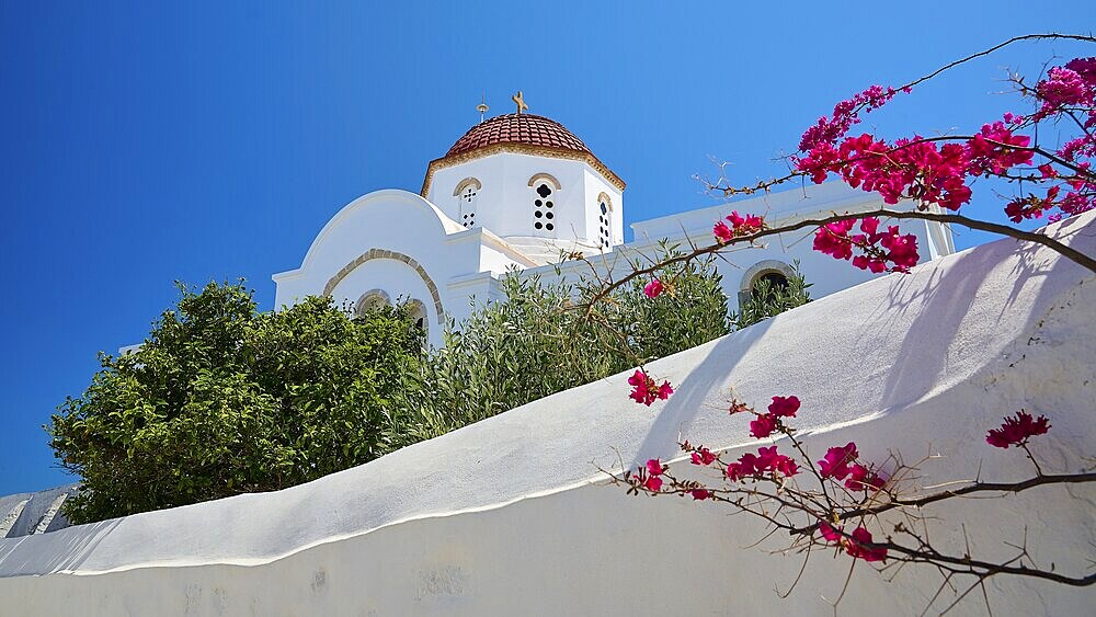 A white wall with a view of a church with a red dome and colourful vegetation under a blue sky, Chora, Old Town, Patmos, Dodecanese, Greek Islands, Greece, Europe