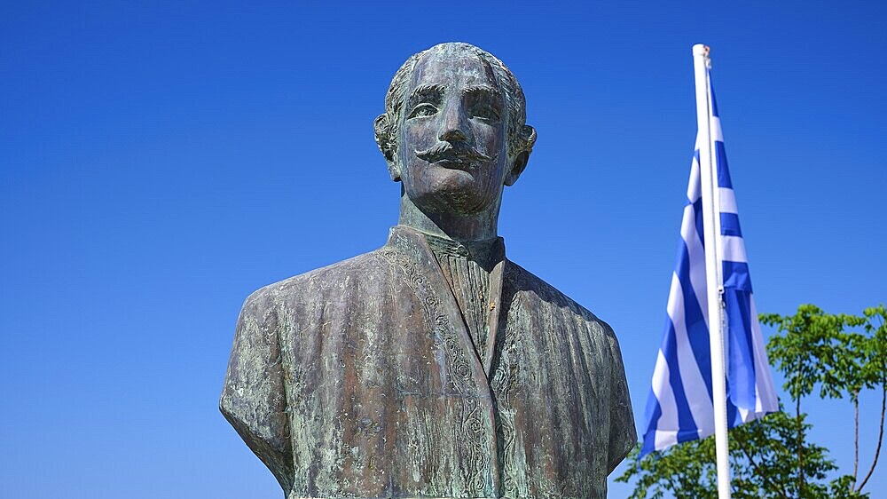 Emmanuel Xanthos, folk hero, bronze statue of a man with a beard next to a Greek flag against a clear blue sky, Chora, Old Town, Patmos, Dodecanese, Greek Islands, Greece, Europe