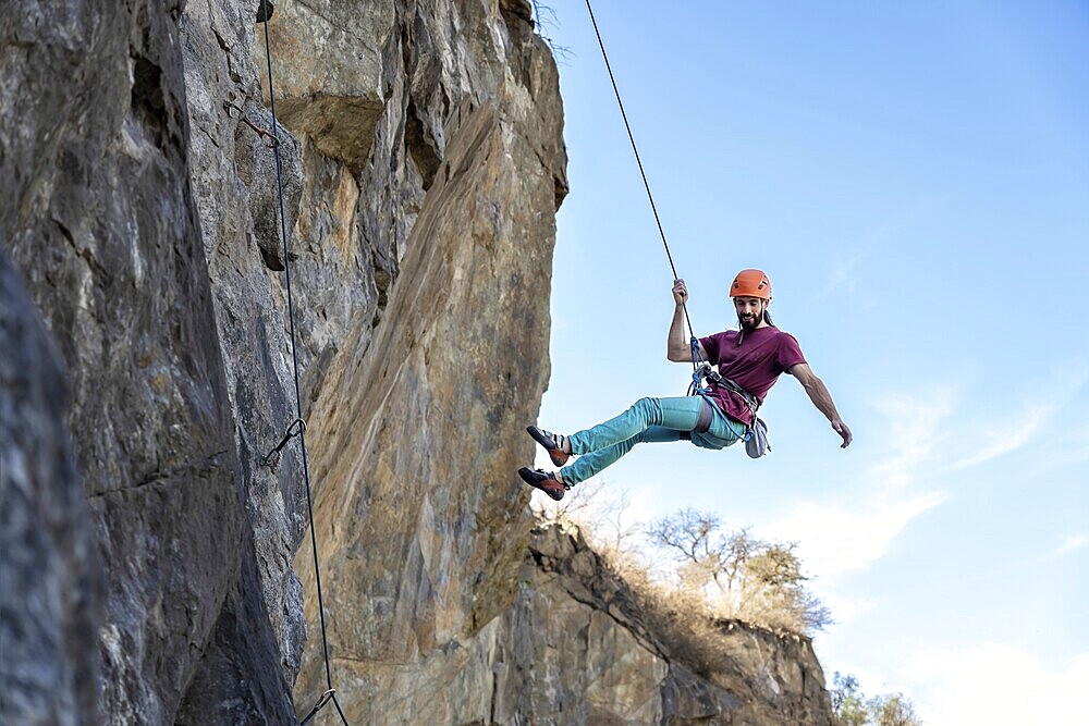 A determined young man ascends a steep cliff, using a rope for support, highlighting his strength and focus as he navigates the challenging rock face, embodying the essence of adventure and perseverance