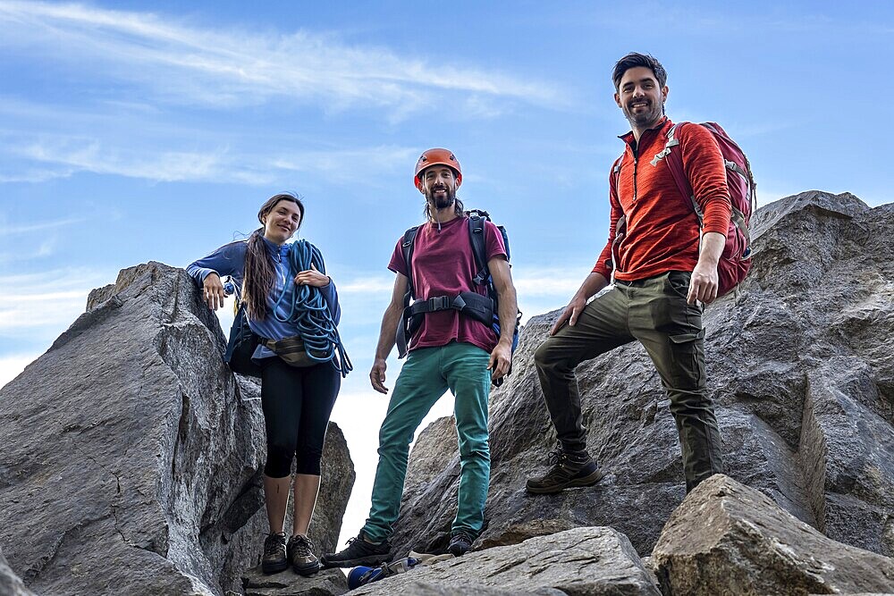 Group of diverse climbers celebrating triumph atop a breathtaking mountain summit, facing camera with joy and achievement. Majestic landscape backdrop under clear skies