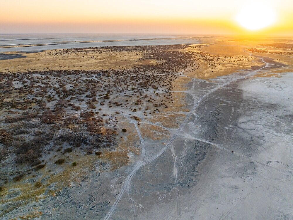 Rocky island with baobab trees in a dry salt pan, at sunset, off-road vehicle on the salt pan, aerial view, Kubu Island, Botswana, Africa