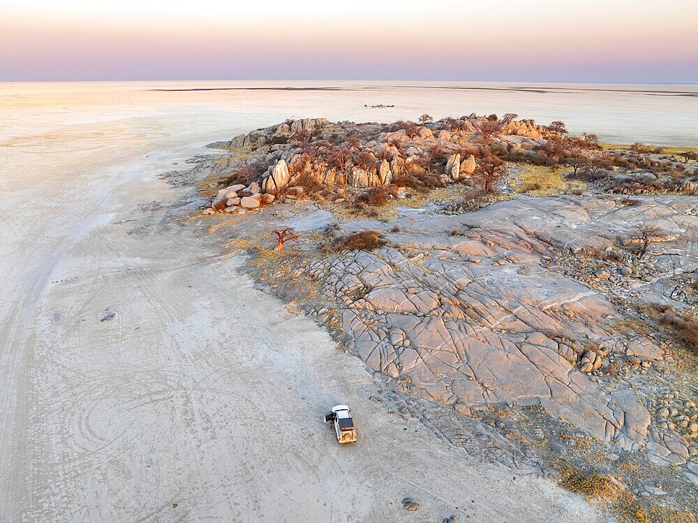 Rocky island with baobab trees in a dry salt pan, at sunset, off-road vehicle on the salt pan, aerial view, Kubu Island, Botswana, Africa