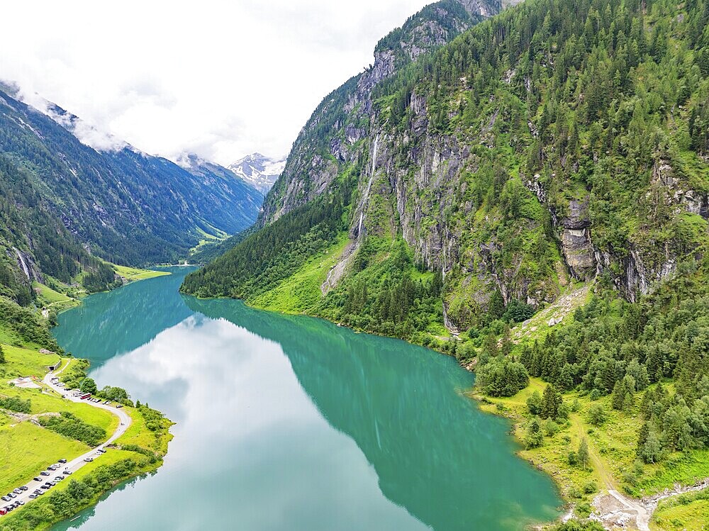 A turquoise-coloured lake nestled in a valley, framed by steep, wooded mountain slopes and cliffs under a cloudy sky, Stilluptal, Austria, Germany, Europe