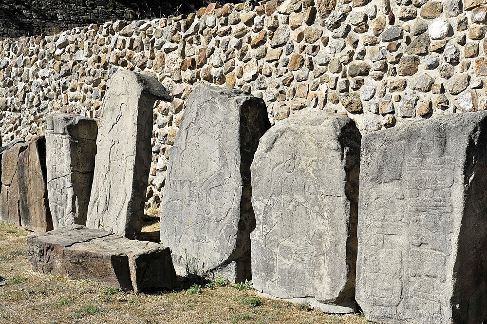 Unesco World Heritage Site Monte Alban, Oaxaca, Mexico, Central America, row of ancient stones with various engravings, lined up in front of a stone wall in the sunlight, Mitla, Central America