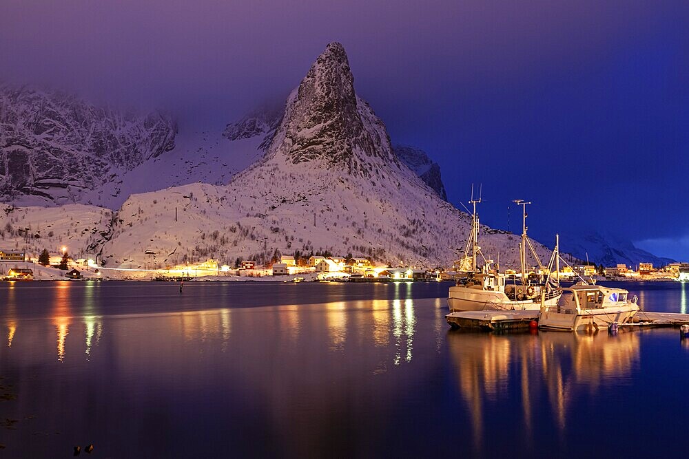 Fishing boats in fjord in front of snowy mountains, illuminated, twilight, winter, Reine, Moskenesoya, Lofoten, Norway, Europe