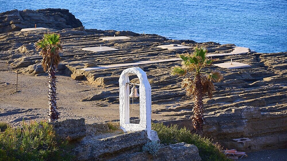 View of a rocky coastline with palm trees, a white bell frame and blue sky in the background, rock church of Agios Nikolaos, Oasis Beach, Kallithea, Rhodes, Dodecanese, Greek Islands, Greece, Europe