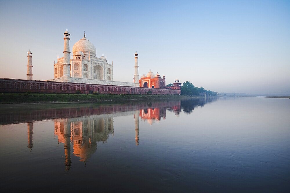 The Taj Mahal glows red at daybreak next to the holy Jamuna river