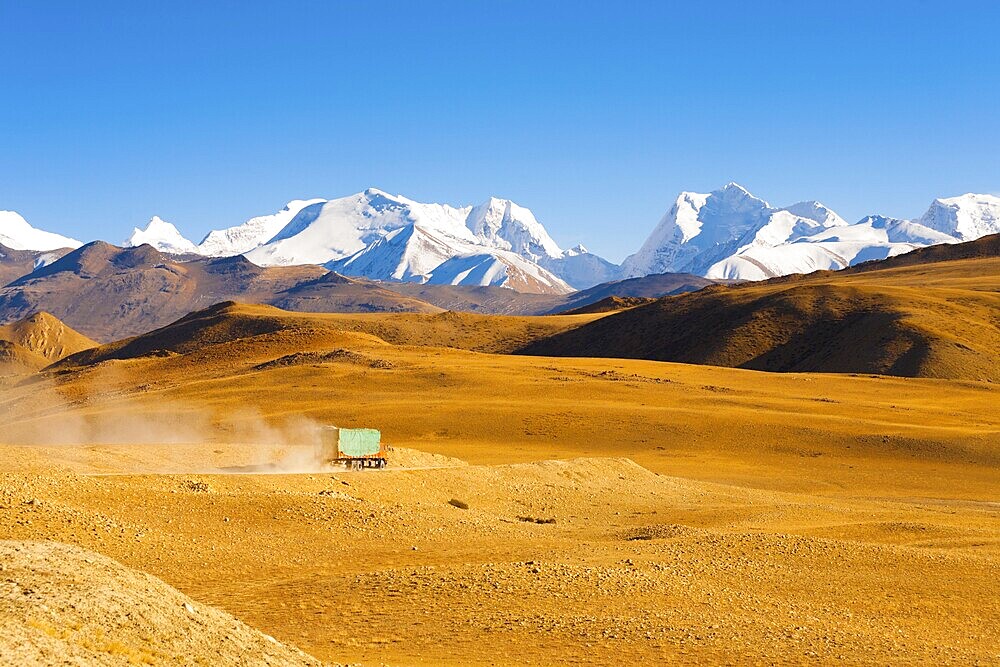 A truck drives through the barren landscape of the mountainous border between Tibet and Nepal as snowcapped himalayan mountain peaks poke through in the distance