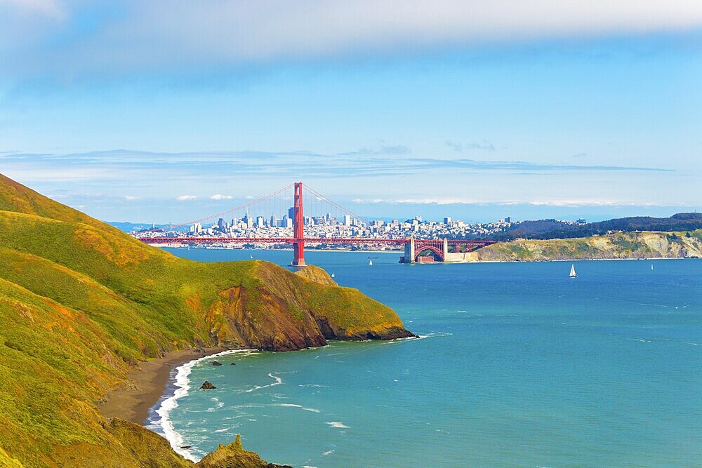 Distant downtown San Francisco cityscape seen through the Golden Gate Bridge together with hills of Marin Headlands in foreground on blue sky day high above the water in California