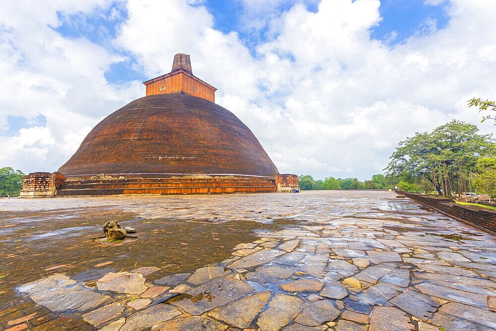 Wet platform of Jetavanaramaya Dagoba or stupa with broken damaged spire seen off centre in the ancient capitol of Anuradhapura Kingdom on a beautiful blue sky day in Sri Lanka