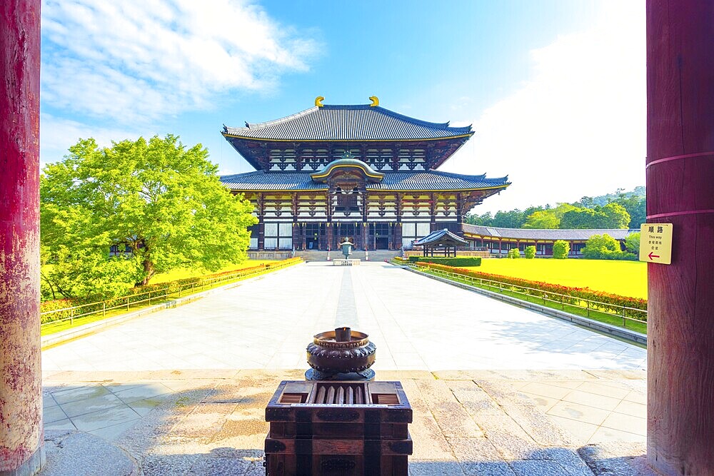 Incense burner and pillars in foreground leading to front facade of the Great Buddha Hall Daibutsuden at Todai-ji temple on a beautiful blue sky morning with nobody present in Nara, Japan. Horizontal