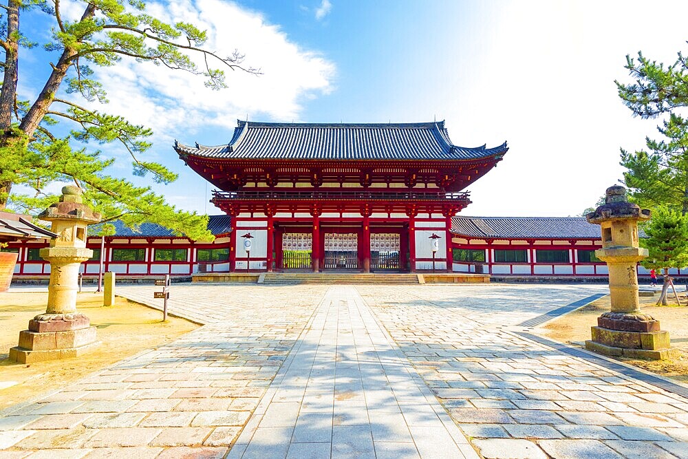 Centered red gate ro-mon front entry to Todai-ji, Todaiji, temple and walkway housing the Daibutsuden on a bright sunny blue sky morning in Nara, Japan. Horizontal copy space