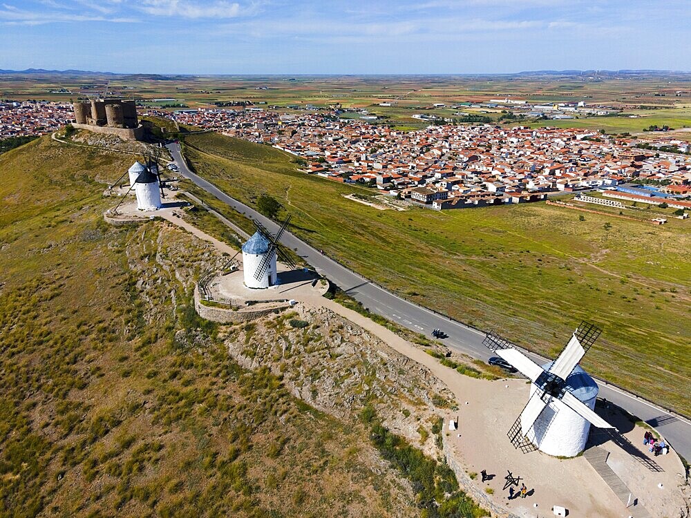 Aerial view of several windmills on a hill next to a road, with a village in the background under a blue sky, aerial view, Consuegra, Toledo, Castilla-La Mancha, Spain, Europe