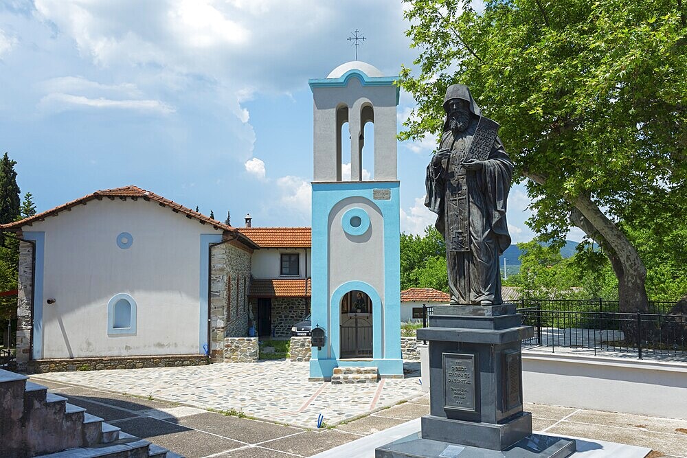 Small church with blue bell tower and black statue in the green courtyard, monument to Agios Siluanos of Athonitos, Panagia Gomatiou church, Gomati, Chalkidiki, Halkidiki, Central Macedonia, Greece, Europe