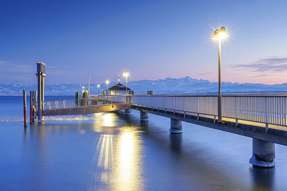 An illuminated jetty over a calm lake with mountains in the background in blue twilight, harbour, Immenstaad, Lake Constance, Baden-Württemberg, Germany, Europe