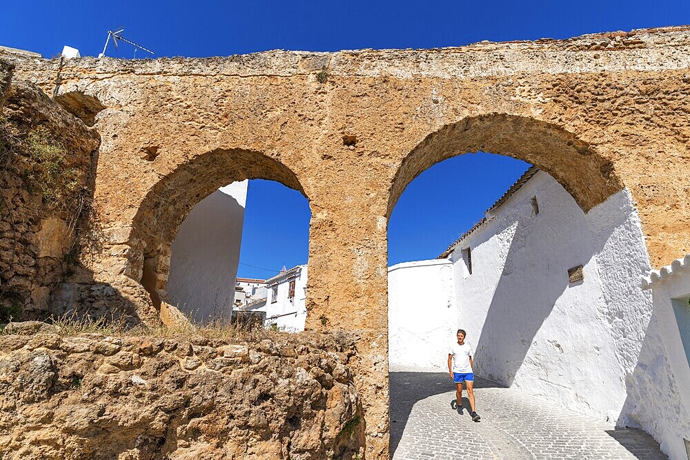 A man walks through an arch under a historic aqueduct in the white village of Yunquera, Sierra de las Nieves National Park, Malaga, Andalusia, Spain, Europe