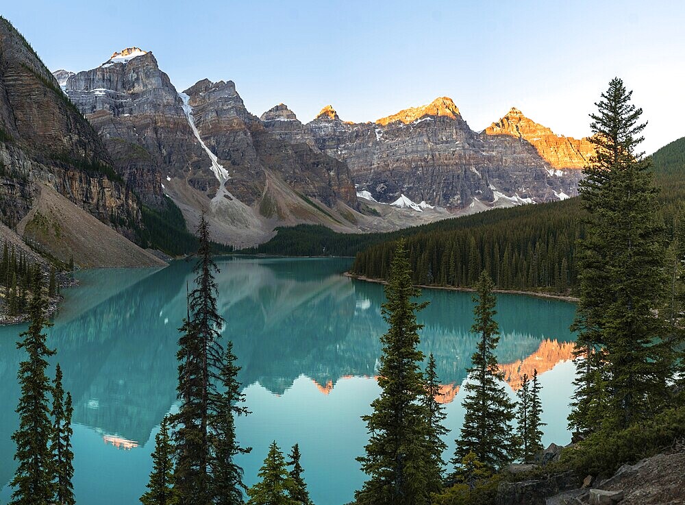Sunset over a serene lake surrounded by rocky mountains and pine trees, with reflections in the clear water, Moraine Lake, Banff National Park, Canadian Rockies