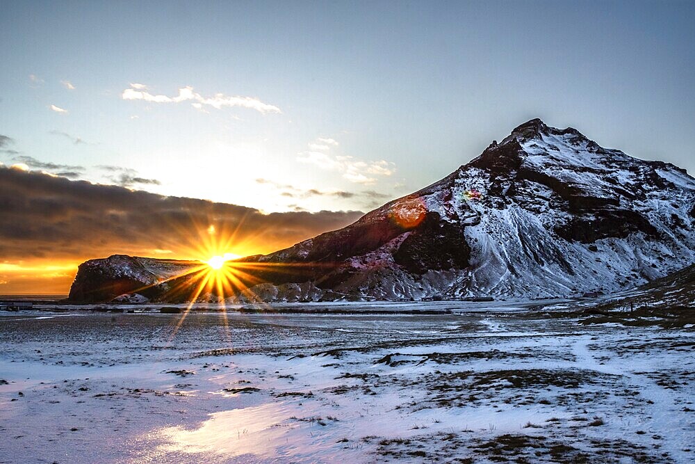 The sun rises behind snow-covered mountains and bathes the wintry landscape in warm light, Iceland, Europe