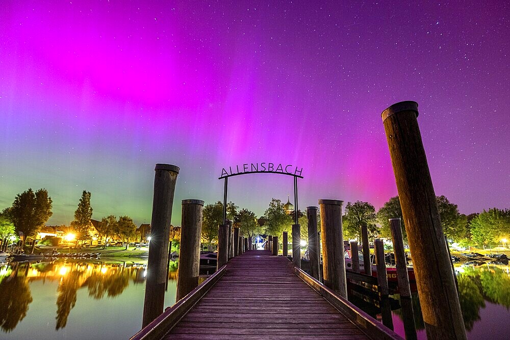 A wooden walkway under a glowing sky with colourful lights and trees with auroras, harbour, Allensbach, Lake Constance, Baden-Württemberg, Germany, Europe