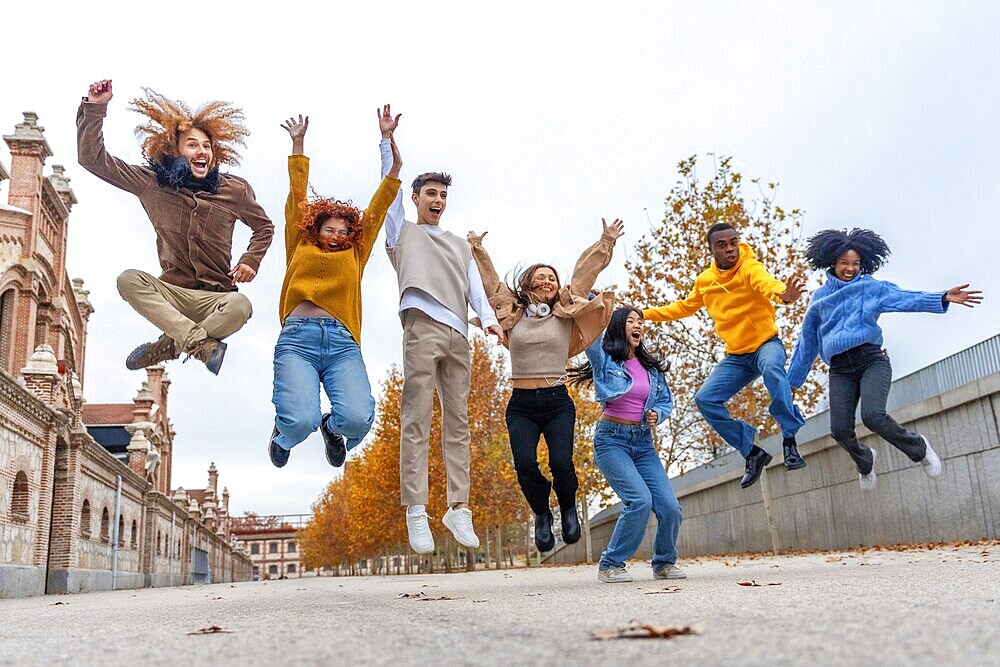 Happy multi-ethnic friends jumping in the street in an autumn day