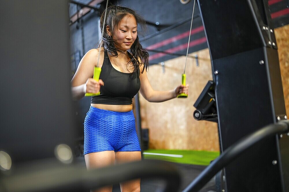 Chinese strong sportive woman exercising pulling weights with lat machine in a cross training gym
