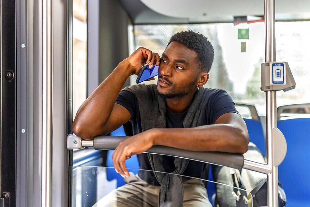 Young african businessman talking to the mobile traveling to the work by bus in the morning