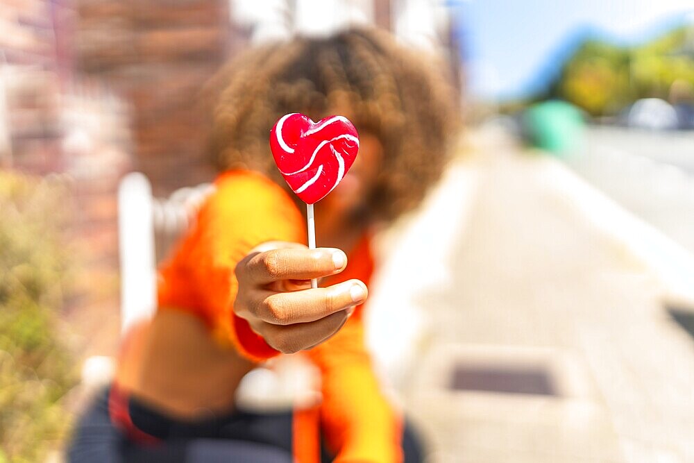 Focus on the hand of a young latin woman holding a heart shape lollipop in the street