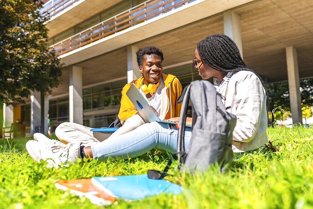 African american students studying with laptop together sitting in the grass outside the campus