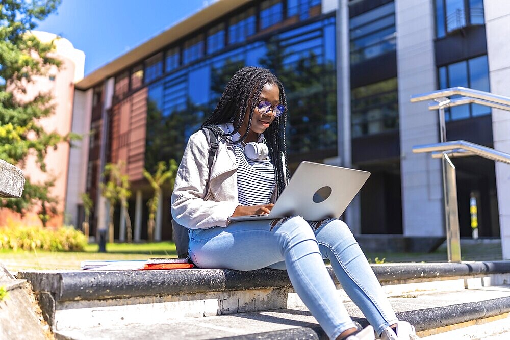 Focused female african university student using laptop sitting on outdoors staircases in the campus