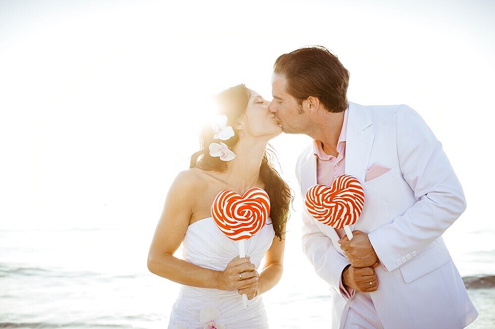 Bride and groom kissing, heart-shaped lollipops in their hands, Spain, Europe
