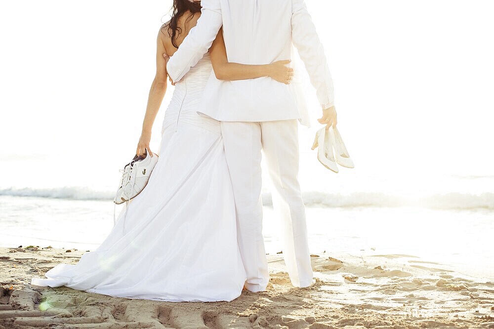 Bridal couple standing arm in arm on the beach, Spain, Europe