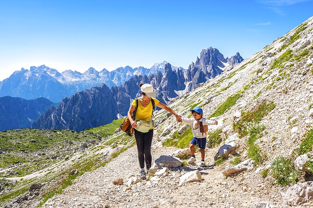 Tourists enjoying a summer hike on a mountain trail in the italian dolomites, with the tre cime di lavaredo peaks in the background