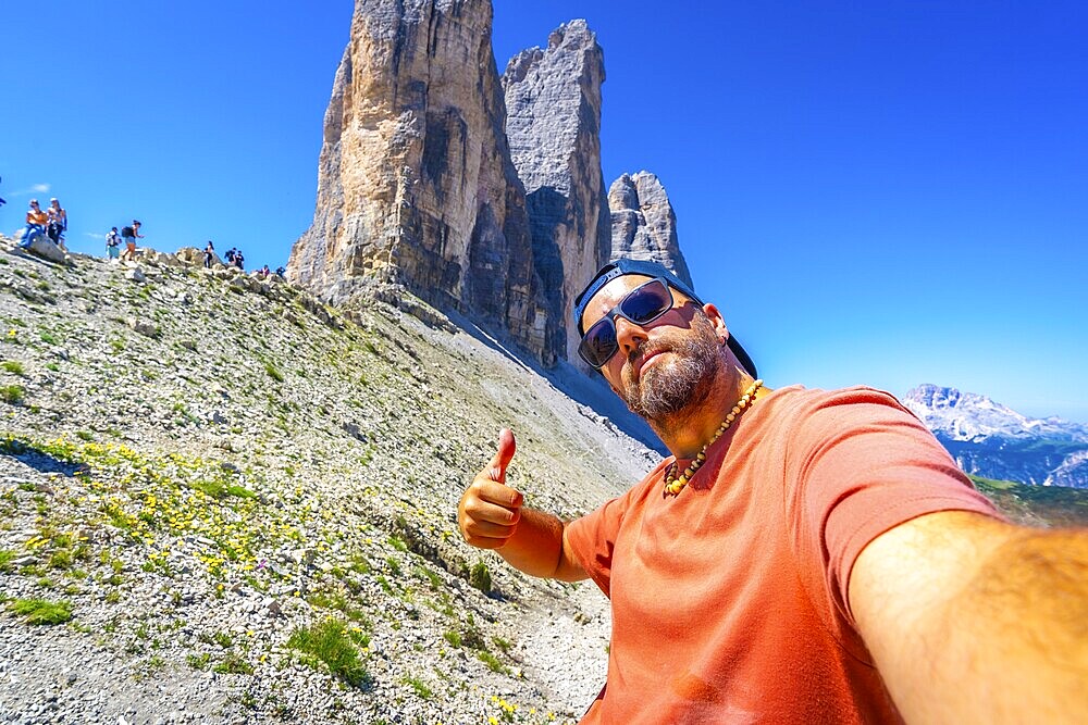 Tourist taking a selfie and making thumbs up gesture while hiking in the tre cime di lavaredo, dolomites, italy, during summer