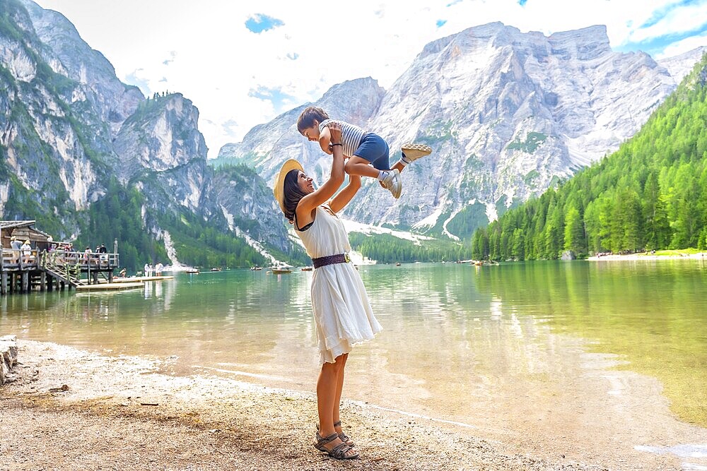 Tourist mother lifting her son in the air while enjoying summer holidays at lake braies, also called pragser wildsee, in the dolomites of italy