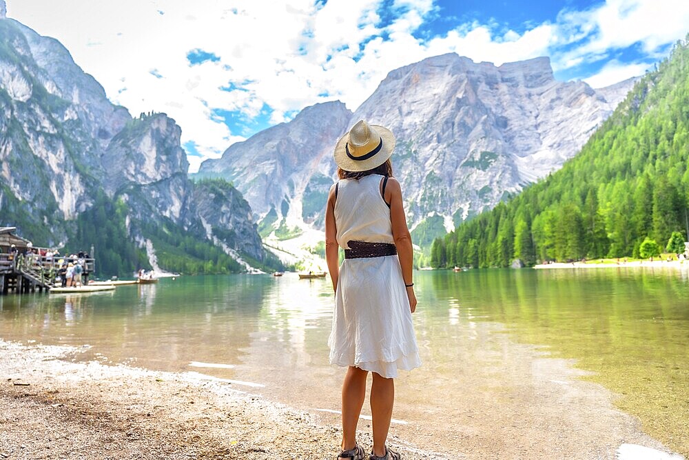 Woman admiring the stunning landscape of lake braies, surrounded by majestic mountains and lush greenery, during a summer day in the italian dolomites