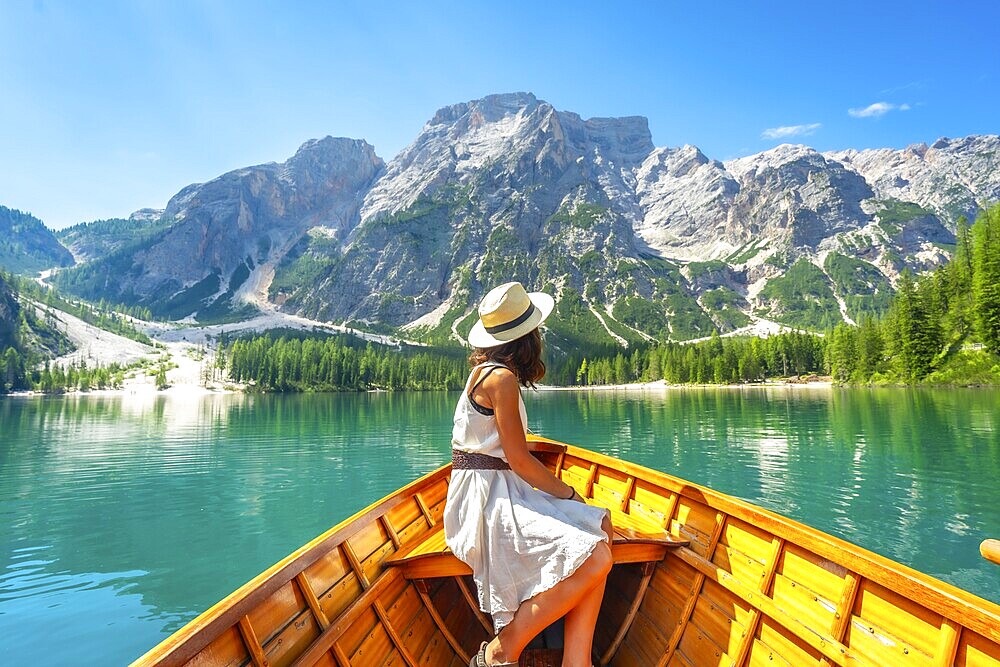 Young woman admiring the stunning landscape of lake braies from a wooden rowboat, surrounded by majestic mountains and crystal clear turquoise water
