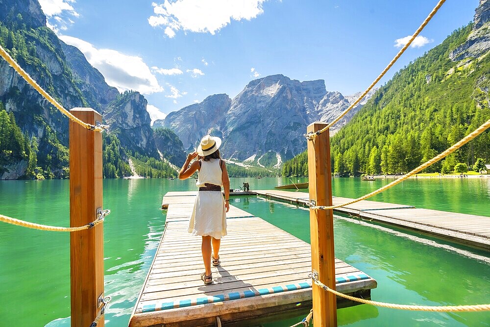 Woman walking along a wooden pier at lake braies, enjoying the turquoise waters and stunning mountain landscape of the dolomites on a sunny summer day