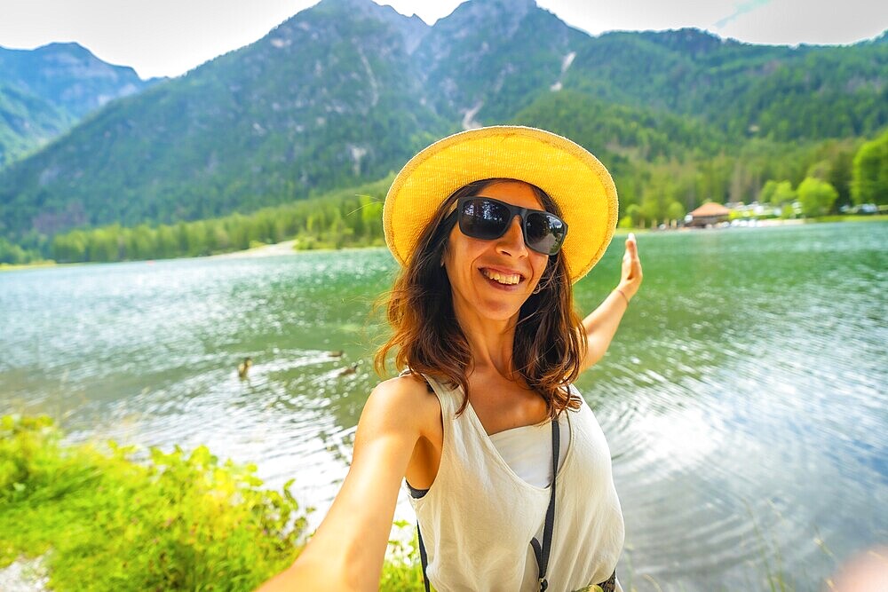 Happy tourist taking a selfie with outstretched arms at lake dobbiaco in the italian dolomites, enjoying summer holidays