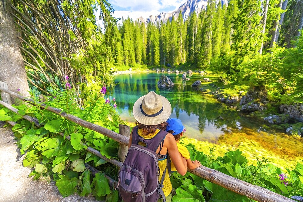 Mother and child enjoying breathtaking view of lake carezza's turquoise waters, surrounded by lush greenery and the majestic dolomites