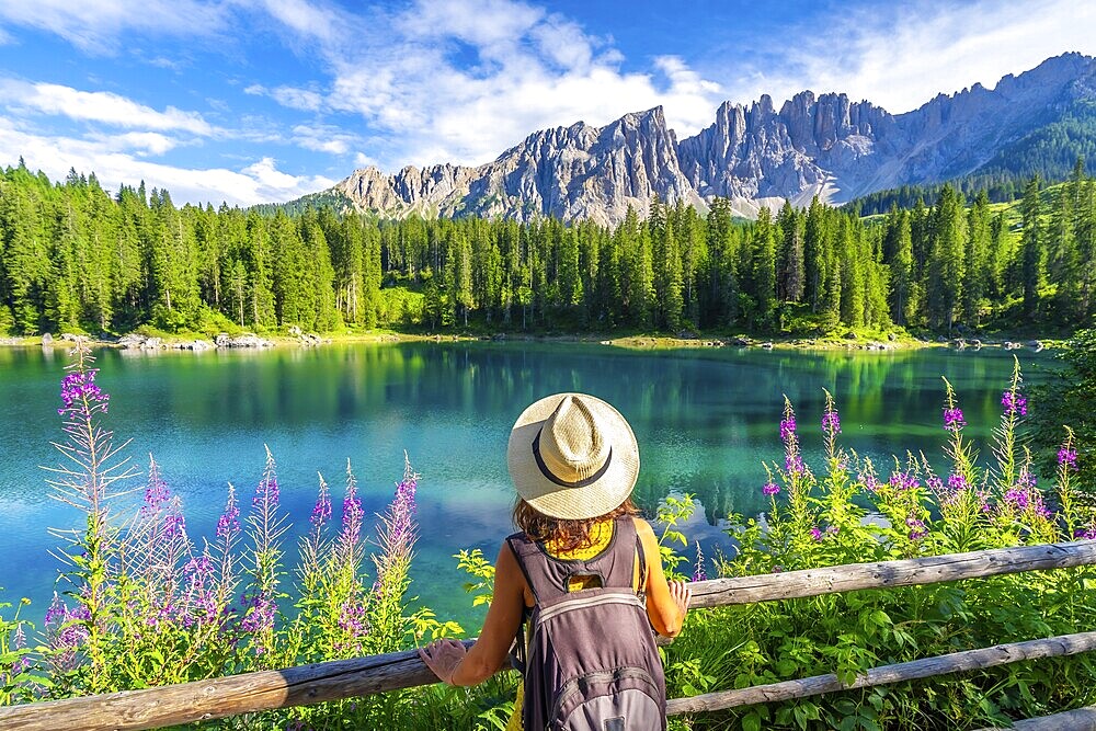 Female tourist admiring the stunning turquoise waters of lake carezza with the latemar mountain range in the background, dolomites, italy