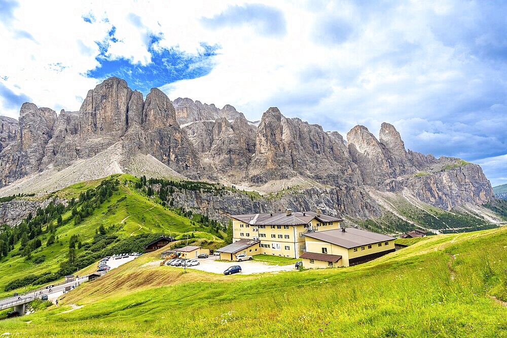 Green meadows and a mountain hotel are surrounded by the breathtaking peaks of the dolomites on a sunny summer day