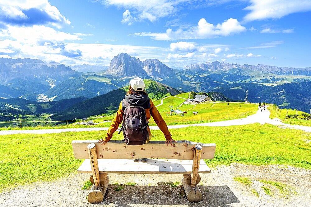 Hiker relaxing on a bench and admiring the odle mountains in val di funes, south tyrol, italy