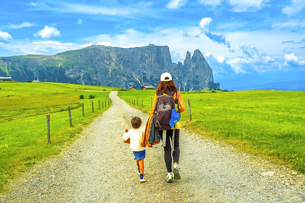 Mother and son walking on a gravel road at alpe di siusi, enjoying summer vacation in the dolomites