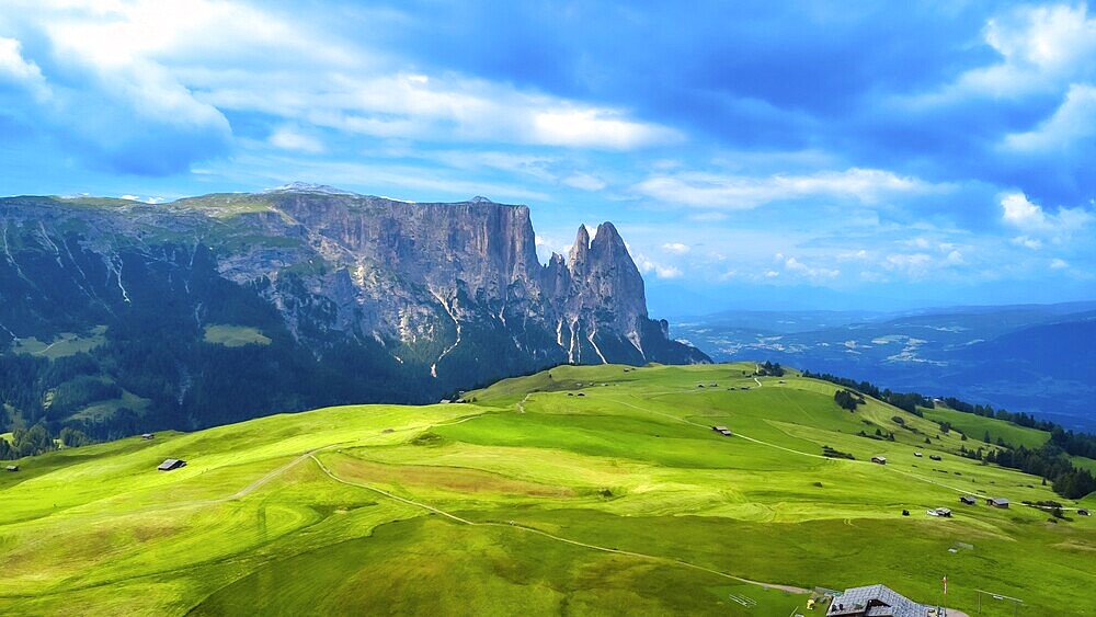 Breathtaking summer landscape featuring lush green meadows, rolling hills, and the majestic peaks of the sassolungo group in the italian dolomites