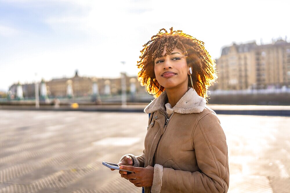Happy beauty latin young using phone and listening to music standing in the city during sunset