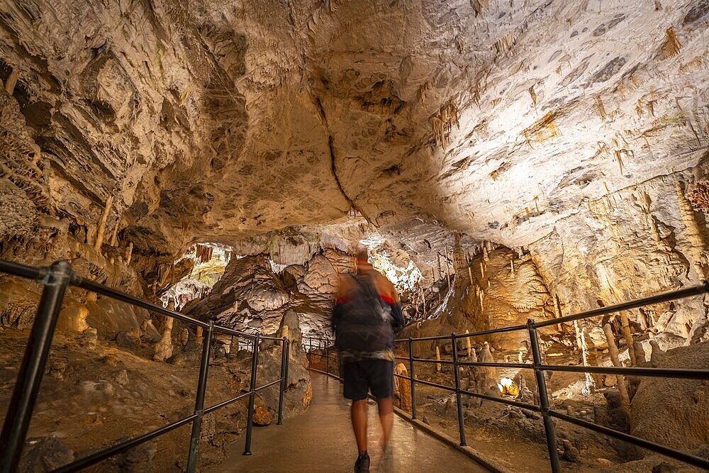 Tourist walking on a concrete walkway inside the famous postojna cave in slovenia, admiring the stalactites and stalagmites during a guided tour