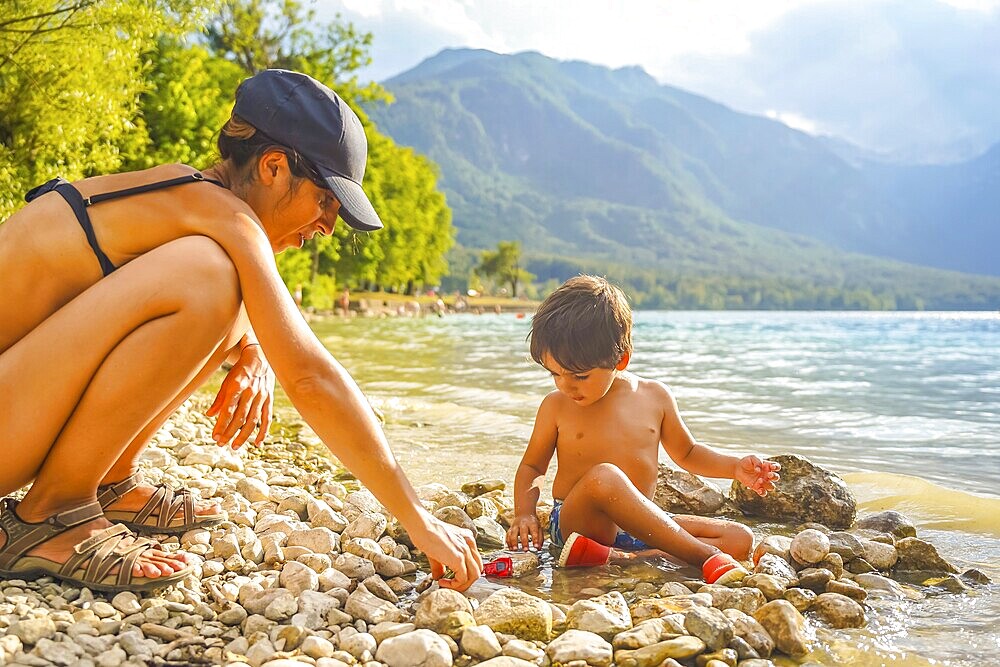 Mother and son enjoying quality time together, playing with pebbles and toy cars on the scenic shores of lake bohinj in slovenia