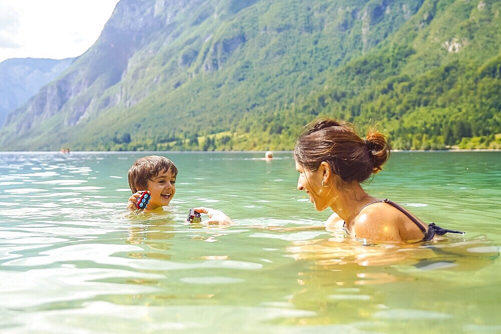 Mother and son enjoying summer fun, playing with toys while swimming in the refreshing waters of lake bohinj, surrounded by the julian alps